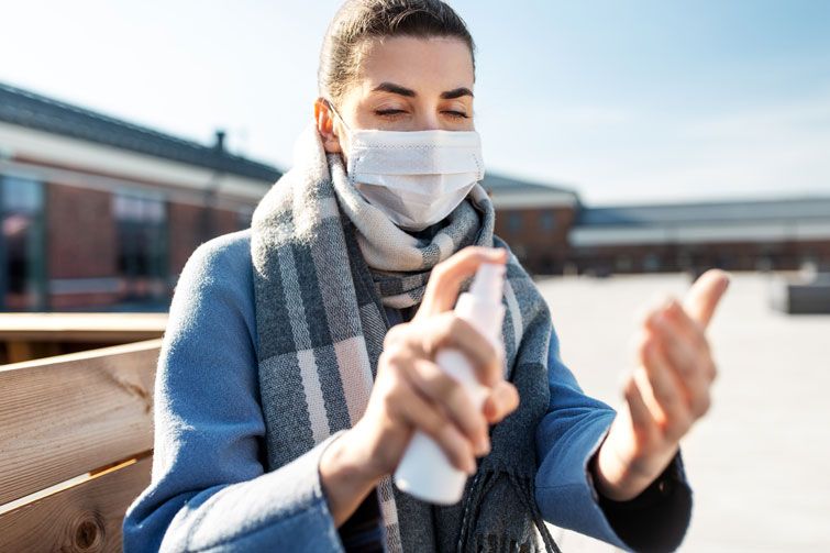 woman in mask spraying hand sanitizer outdoors
