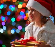 Cute girl in Santa cap holding giftbox on sparkling background